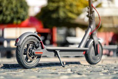 Elektrikli scooter fayanslı kaldırıma park edilmiş. Arka tekerin yakın çekim detaylarında disk freni var.