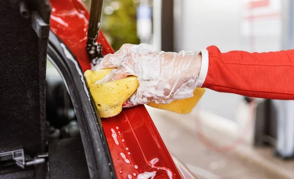 Jovem mulher limpeza parte traseira de seu carro, close-up detalhe na mão em luva segurando esponja amarela — Fotografia de Stock