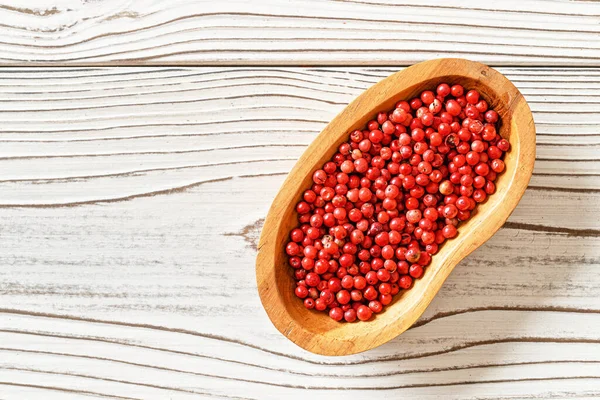 Red or Pink peppercorn in small wooden bowl, on white boards desk, closeup photo from above