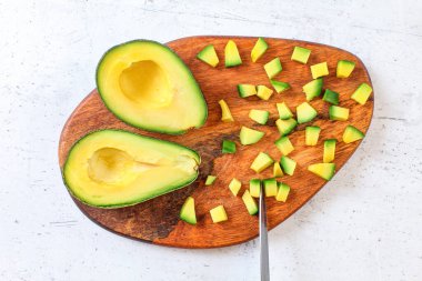 Sarı yeşil avokado hamuru, tahta kesme tahtasının üzerinde küçük parçalara ayrılmış, yanında bıçak, yukarıdan görüş.