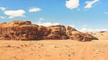 Rocky Massifs kırmızı kum çölünde, araç zemini izler, arkaplanda parlak bulutlu gökyüzü, tipik Wadi Rum manzarası, Ürdün
