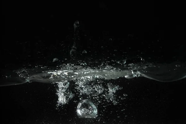 Water splashing, forming bubbles as it\'s poured into aquarium tank, black background