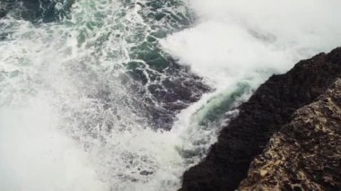Kayalık kıyıya vuran deniz, sıçrayan yeşil su, yukarıdan görünen beyaz köpük, yavaş çekim videosu