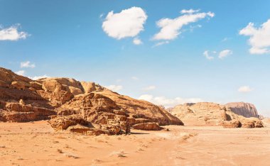 Rocky Massifs kırmızı kum çölünde, araç zemini izler, arkaplanda parlak bulutlu gökyüzü, tipik Wadi Rum manzarası, Ürdün