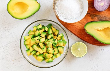 Avokado yarımları, limonlar ve soğan, biraz tuz - beyaz çalışma tahtasında temel guacamole malzemeleri, yukarıdan görünüm