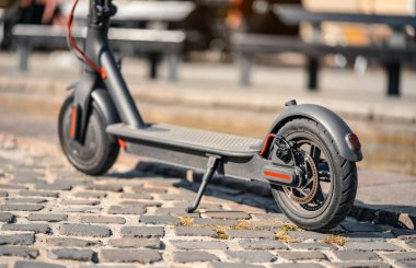 Elektrikli scooter fayanslı kaldırıma park edilmiş. Arka tekerin yakın çekim detaylarında disk freni var.