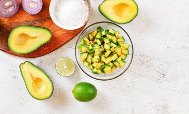 Avokado yarımları, limonlar ve soğan, biraz tuz - beyaz çalışma tahtasında temel guacamole malzemeleri, yukarıdan görünüm, metin sağ tarafında boşluk