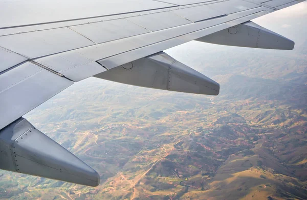 View from passenger window of commercial airplane, blurred mountainous African landscape visible under aircraft wing