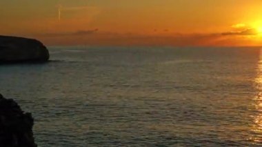 Sabah turuncu güneş sakin denizin üzerinde yükseliyor, kayalık kıyı solda, zaman kavramlı video