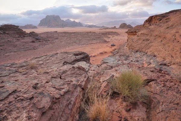Red sandstone rocks formations with few dry shrubs or bushes in Wadi Rum (also known as Valley of the Moon) desert, Jordan. Clouds over mountains background