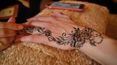 Genç bir kadın geçici kına dövmesini yaptırıyor. Mürekkep hala kalın ve ıslak. Sadece yakın çekim detaylarıyla.
