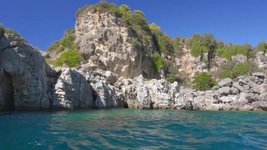 Keskin yüksek kayalık kayalıklar ve açık yeşil suyun üzerinde görünen kozalaklı ağaçlar - Liapades, Korfu Yunanistan yakınlarındaki tipik deniz manzarası, bir tekneden görülüyor