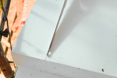 İnşaat işçisi, polistiren köpük ısı yalıtımını el testeresiyle kesiyor.