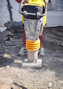 İnşaat alanında çakıl sıkıştırıcı ya da taşınabilir titreşim kesici kullanan sanayi işçisi, makinede detay