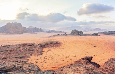 Ürdün Wadi Rum Çölü 'ndeki manzara gibi kırmızı turuncu Mars. Dağların arkaplanı bulutlu sabah, küçük araç mesafesinde. Bu konum birçok bilim kurgu filminde kullanılmıştır.