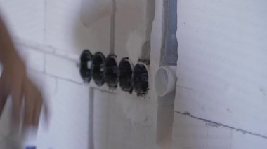 Elektrik kablosu için plastik boruyu yerleştiren inşaat işçisi çıplak duvarın içindeki kanalları kovalıyor.