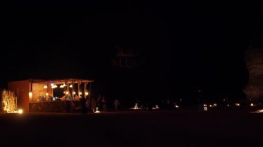 Alula, Suudi Arabistan - 4 Mart 2023: Yerel halk ve turistler Jabal AlFil yakınlarındaki küçük bir dükkandan kahve satın alıyorlar - Fil Kayası, akşam manzarası aydınlanıyor, insanlar için yerde koltuklar kuruluyor