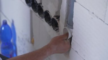 Elektrik kablosu için plastik boruyu yerleştiren inşaat işçisi çıplak duvarın içindeki kanalları kovalıyor.