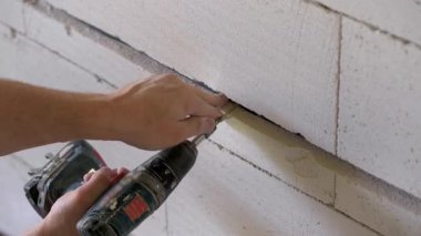 Elektrik kablolarını oyukta güvence altına alan ya da yeni inşa edilmiş bir evin duvarında elektrikli matkap ve vida kullanarak kovalayan bir elektrikçi. Kapatma ayrıntısı.