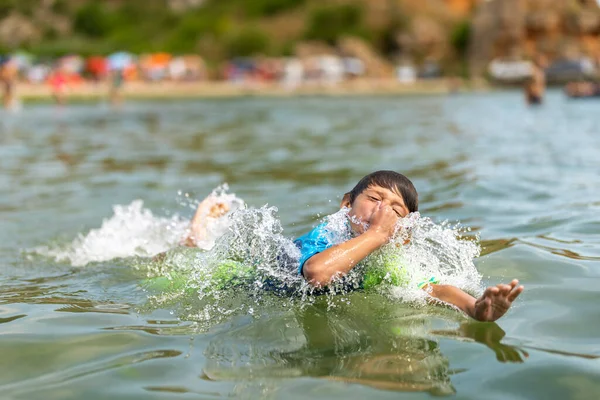 सुंदर लहान मुलगा समुद्रात खेळत आणि पोहत, त्याचे नाक धारण करीत, सुमारे पाणी स्प्लॅश करीत आहे स्टॉक पिक्चर