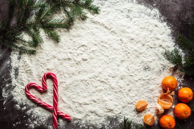 Mandalinalar ve Noel ağacı dallarıyla masaya saçılmış un üzerinde lolipoplar.