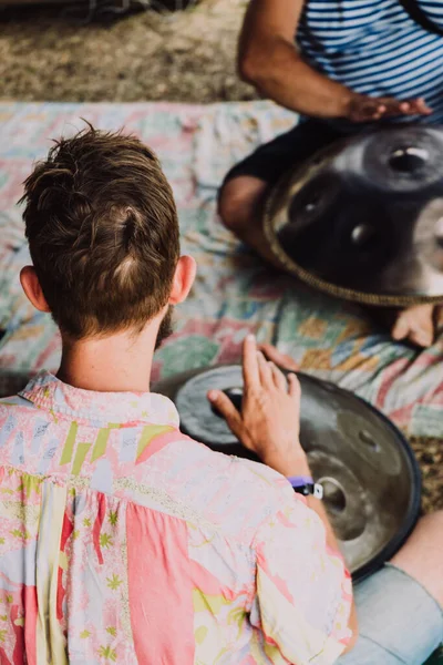 men playing ethnic musical percussion instrument big metal drum at festival outdoors sitting on floor 1