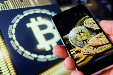 Cep telefonu tutan adam, bitcoin simgesi, borsa arkaplanı grafikli blok zinciri, kripto para birimleri veya bitcoin konsepti