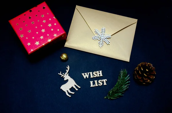 Wunschliste Holzbuchstaben auf schwarzem Hintergrund mit Weihnachtsdekoration. Goldener Umschlag und roter Geschenkkarton auf dunklem Hintergrund. Weihnachtskonzept. — Stockfoto