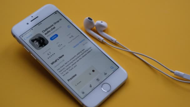 Tonbridge, Velká Británie - 19.02.2021: Clubhouse app na displeji iPhone, ruka bere bílé sluchátka ze žlutého pozadí. Bílé, žluté barvy. Zobrazení aplikace Clubhouse audio chat na smartphonu. — Stock video