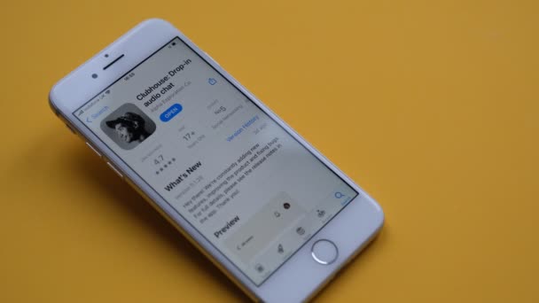 Tonbridge, Storbritannien - 27.02.2021: Klubbhusappen på iPhoneskärmen med trådlösa headset på gul bakgrund. En hand lägger ner ett headset. Clubhouse audio chat program visa på smartphone. — Stockvideo