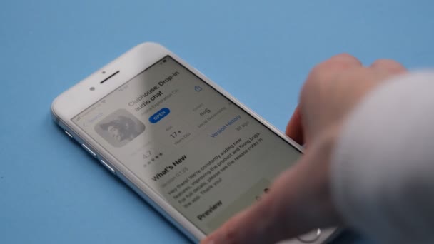 Tonbridge, UK, 17.02.2021, Ansicht der Clubhouse-Anwendung auf dem Smartphone. Hand nimmt iPhone vom Tisch auf blauem Hintergrund. — Stockvideo