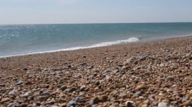 Çakıl taşı İngiliz plajı, seçici odaklanma. Çakıl taşı renkli kıyı şeridi, yatay. Dalgalar çakıl taşı plajına ulaşıyor. Gökyüzü, yatay çizgi, dalgalar ve çakıl taşları. Dungeness Burnu, Kent, İngiltere.