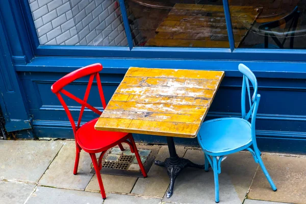street photography, old wooden table with two chairs red and blue colors. Street style cafe. Empty table on the street.