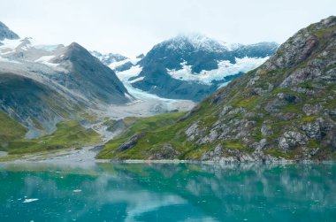 Alaska bulutlu arazi dağları ve su. Dağlar suda yansıyor. Uzaktan kumandalı, fişi çekilmiş. Doğadaki vahşi güzellik. Dokunulmamış ortam. 