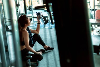Kadın spor salonunda antremandan sonra mola verip su içiyor..