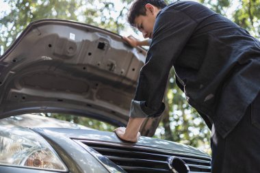 Ormanda yolda kırık bir arabanın kaputunu açan adam. Araba arızası kavramı.