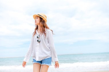 Hasır şapkalı ve kumsalda yürüyen bir kadın..