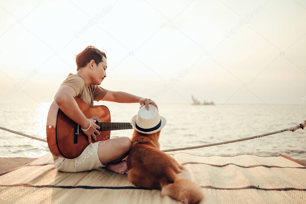 A man play guitar music song near the sea sunset and try wearing hat in dog head