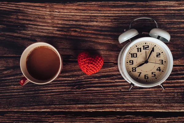 Alarm clock, heart shape and coffee on wood table.
