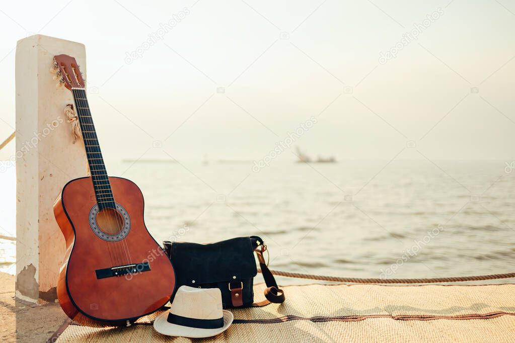 Hat, Bag and Guitar on reed mat near the sea at sunset. Travel, vocation, holiday, summer concept.