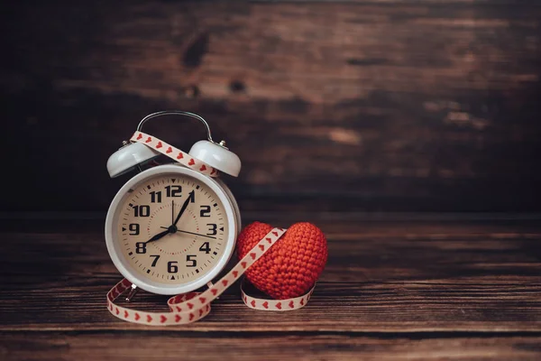 Alarm clock and heart shape on wood table.