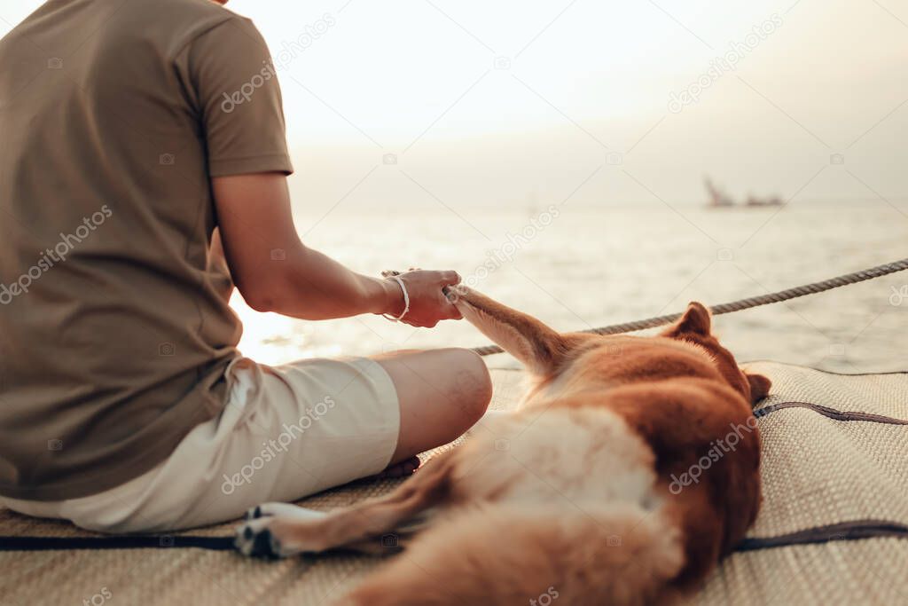 A man hold one hand  with a dog pet near the sea sunset