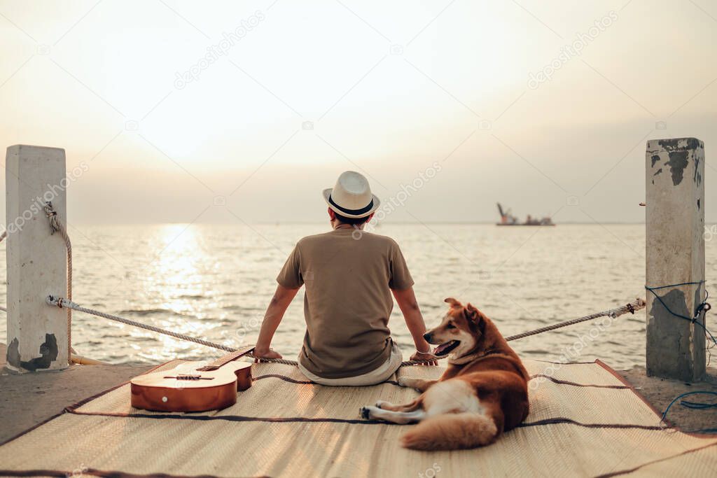 A man wear straw hat and hug with a dog relax near the sea sunset