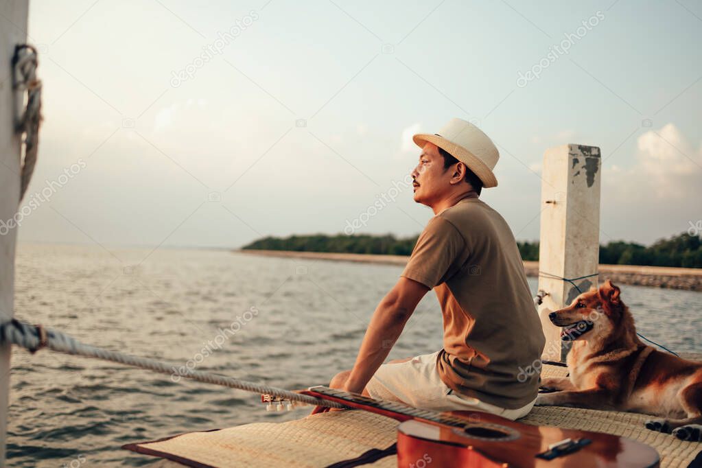 A man wear straw hat and hug with a dog relax near the sea sunset