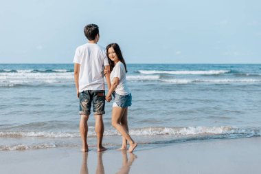 Romantik çift el ele tutuşup sahilde yan yana durur. Aşık bir adam ve kadın.