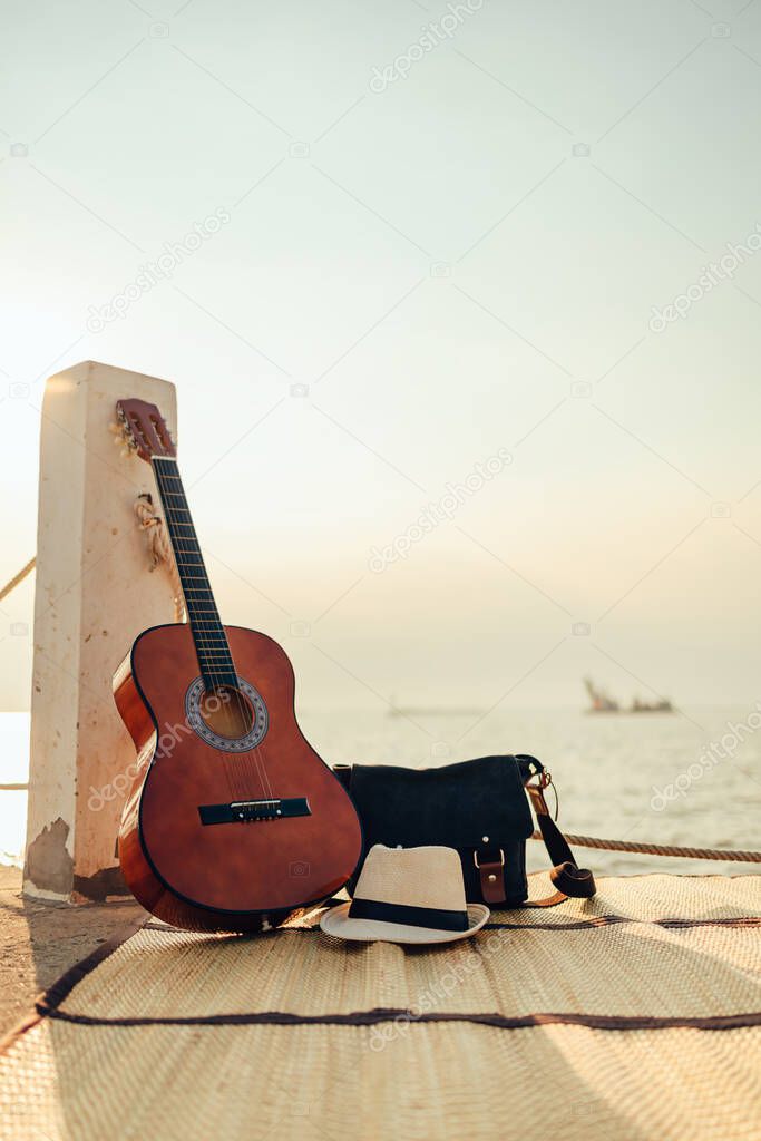 Hat, Bag and Guitar on reed mat near the sea at sunset. Travel, vocation, holiday, summer concept.