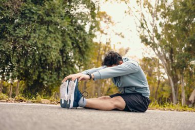 Genç adam koşmadan önce parkta geriniyor. Genç adam parktaki fitness antrenmanından önce antrenman yapıyor. Sağlıklı ve egzersiz yapan genç adam ormanın yanındaki yolda ısınıyor..