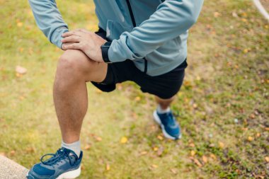 Çekici genç adam koşmadan önce parkta geriniyor. Genç adam parktaki fitness antrenmanından önce antrenman yapıyor. Sağlıklı ve egzersiz yapan genç adam ısınıyor..