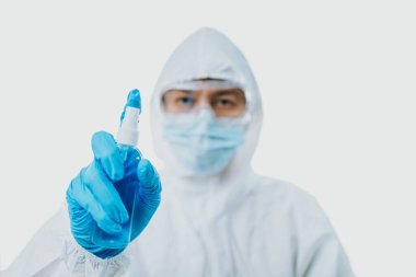 Doktor elinde alkol şişesi tutuyor ve COVID-19 enfeksiyonunu korumak için kişisel koruyucu ekipman ya da maske, gözlük, tıbbi eldiven ve takım elbise giyiyor. Coronavirus, tıbbi ve sağlık hizmetleri kavramı