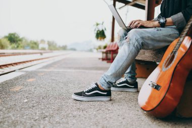 Genç Asyalı adam dizüstü bilgisayarını tren istasyonunda çalışmak ve seyahat yeri aramak için kullanıyor. Serbest çalışma ve seyahat kavramı.